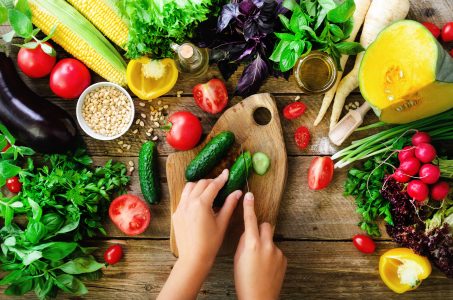 Woman hands cutting vegetables on wooden background. Vegetables cooking ingredients, top view, copy space, flat lay